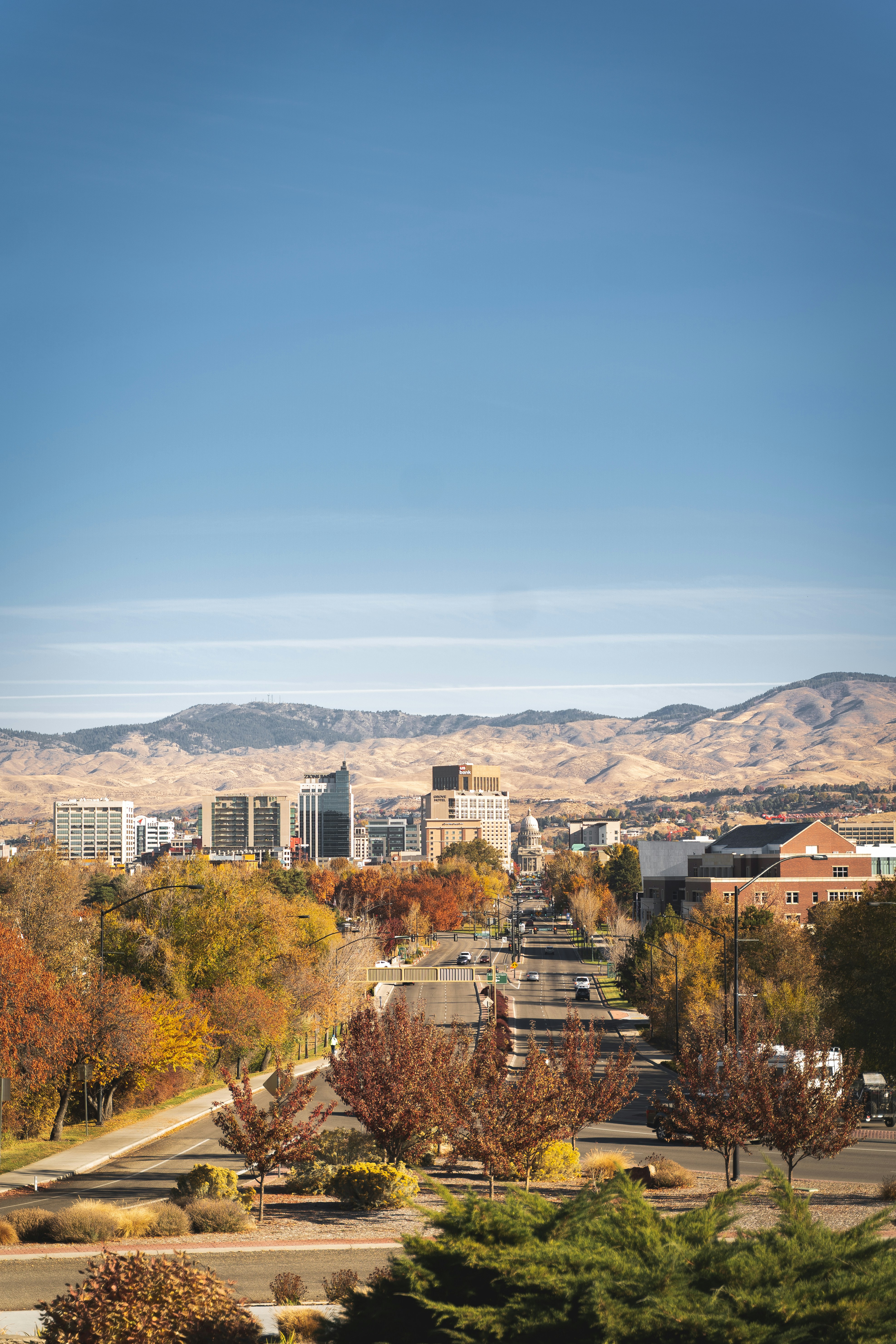 View down Capitol Boulevard toward the downtown Boise skyline and foothills framed by autumn foliage.